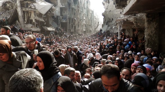 epa04101663 An undated handout picture made available on 26 February 2014 by the United Nation Relief and Works Agency (UNRWA) shows Palestinian and Syrian residents of Yarmuk Palestinian Refugee Camp crowding in a destroyed street as food is distributed, in Damascus, Syria. EPA/United Nation Relief and Works Agency / HANDOUT HANDOUT EDITORIAL USE ONLY/NO SALES